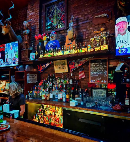 Gabriel's Gate full bar showing extensive spirits wall, stained glass windows, Buffalo Bills jersey, vintage trophies and chalkboard beer list at Allen Street Buffalo NY