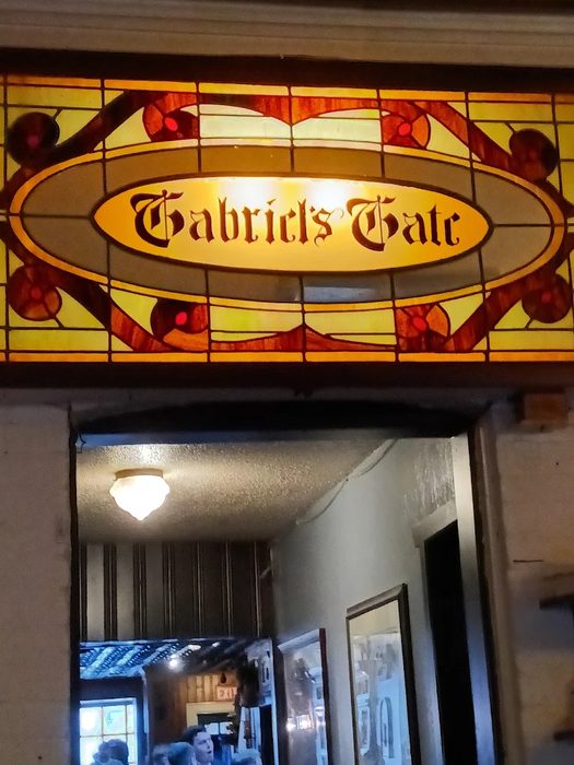 Beautiful vintage stained glass window above the entrance reading Gabriel's Gate in gothic lettering with amber and red floral patterns at the Allen Street tavern in Buffalo NY